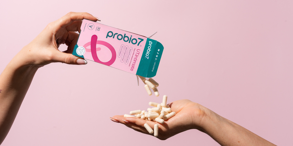Hands holding UTI probiotics and their packaging against a pink background