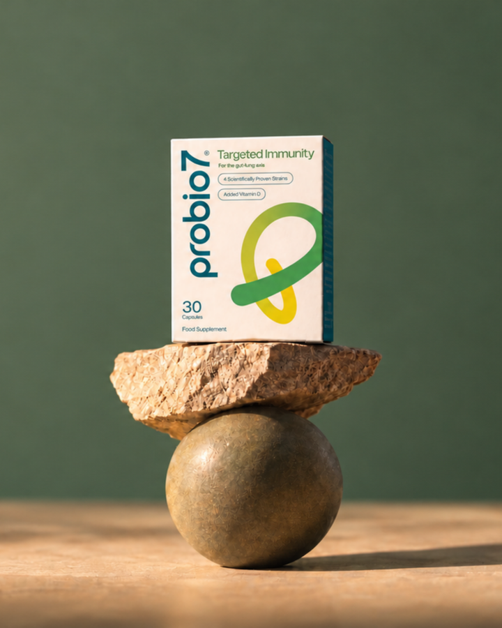 A box of Probio7 Targeted Immunity Probiotics stands upright on stacked natural stones against a muted green background.