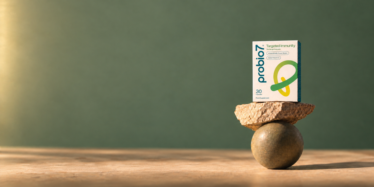 A box of Probio7 Targeted Immunity Probiotics stands upright on stacked natural stones against a muted green background.